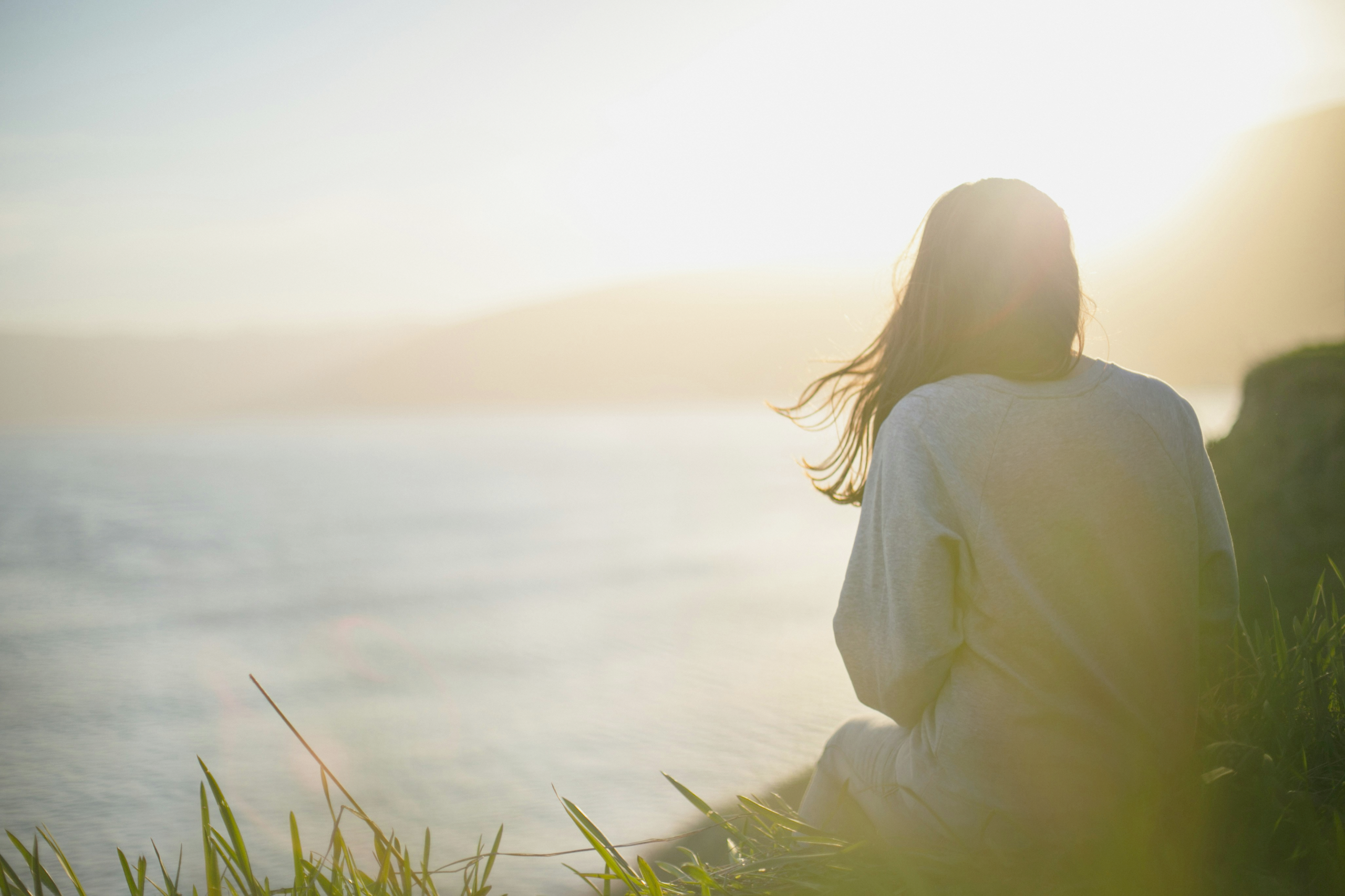 A woman sitting quietly by the sea in soft morning light